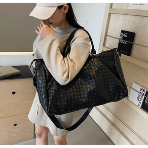 Close-up of black woven leather travel tote featuring detachable woven shoulder strap