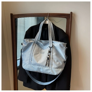 Detail of light blue nylon tote bag with shoulder strap styled on a black suit blazer