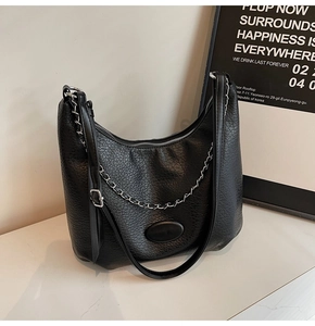 Detail of black lychee grain PU crossbody bag featuring matte oval hardware and silver chain