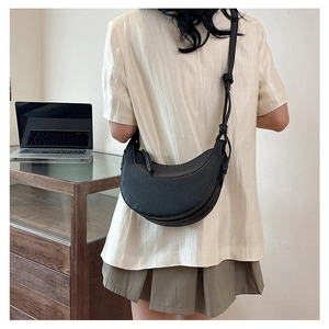 Foto lifestyle di una borsa a tracolla nera a mezzaluna con trama litchi sulla modella
