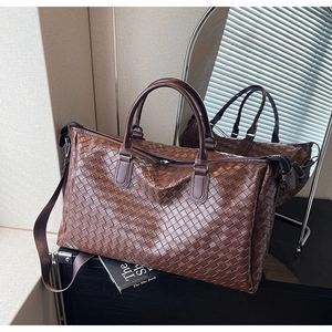 Detail of premium brown woven leather travel bag with dual handles and metal zipper hardware