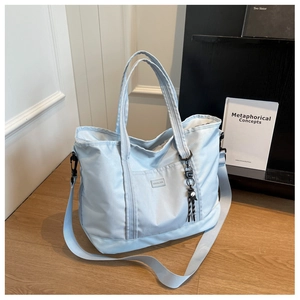 Light blue large travel tote bag featuring wide shoulder strap and black doll pendant