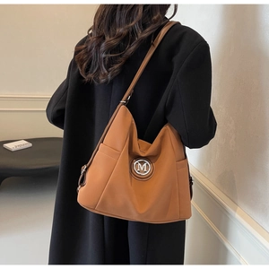 Detail of camel leather tote bag with silver M logo shown on model for size and fit