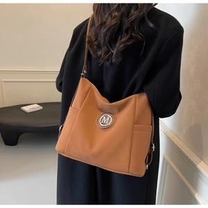 Detail of caramel tote bag showing the side pocket and metallic M logo on premium leather