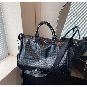 Detail shot of black woven leather travel bag with detachable wide nylon shoulder strap