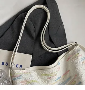 Detailed view of white textured tote with colorful wavy embroidery and smooth long strap