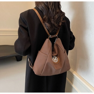Detailed view of the brown nylon backpack featuring a metallic M logo and side pocket