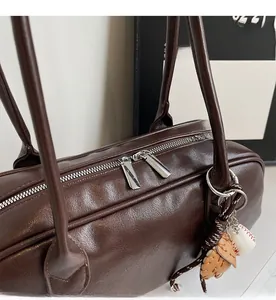 Detail of smooth double silver zippers on dark brown leather shoulder bag with baseball charm