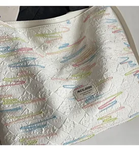 Close-up of off-white tote bag with embossed texture and colorful stitching details