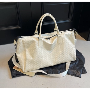 Detail of woven leather travel bag showing texture, dual handles and wide shoulder strap