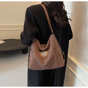 Brown large capacity tote bag with metal M logo shown on model back shoulder view