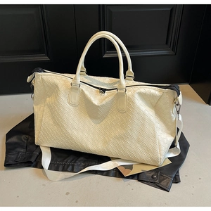 Detailed close-up of woven cream leather travel bag with detachable strap and top handles