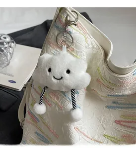 Close-up of a plush white cloud charm with cute embroidery on a textured tote bag