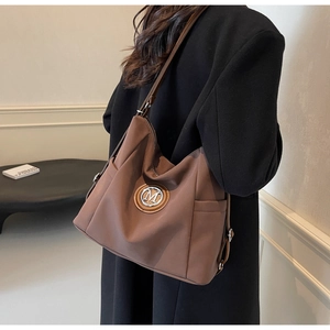 Close-up of brown nylon tote bag featuring metallic M logo and adjustable shoulder strap