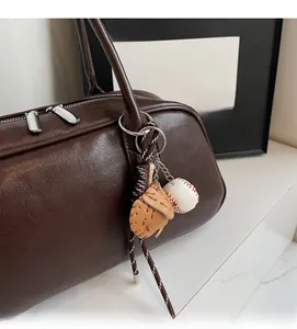 Detailed close-up of a baseball glove pendant and ball charm on a dark brown leather bag