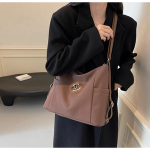 Detail of a brown tote bag featuring a silver M logo and an adjustable shoulder strap