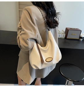 Dettaglio borsa hobo in pelle color crema con catena argento indossata su un blazer