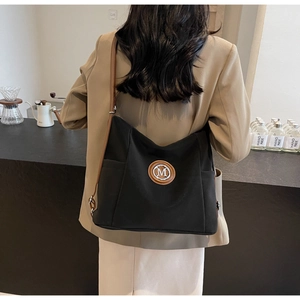 Detail of minimalist black canvas tote with leather M logo and shoulder strap worn by model