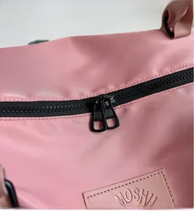 Close-up of pink nylon travel bag featuring smooth black double zippers and leather logo patch