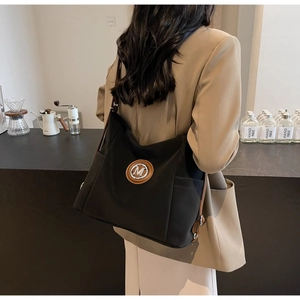 Macro shot of the black canvas tote bag with brown leather M patch and metal detail
