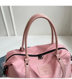 Detail of pink travel bag showing round handles, black zipper, and brand patch