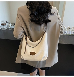 Dettaglio borsa hobo beige con trama litchi e tracolla a catena indossata da modella