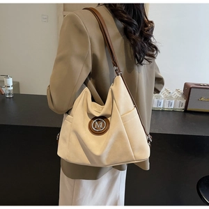 Close-up of minimalist tote bag featuring a circular metal M logo and brown leather straps