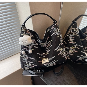 Close-up of black tote bag featuring colorful wavy embroidery and a cloud plush charm