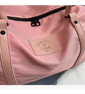 Detail of pink nylon travel bag featuring metal double zippers and leather logo patch