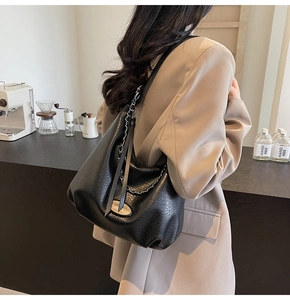 Detail of black pebbled leather tote bag with silver chain strap and oval leather tag