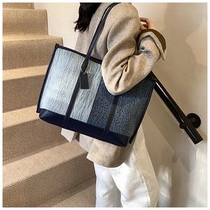Detail of blue patchwork tote bag featuring denim textures and smooth leather straps