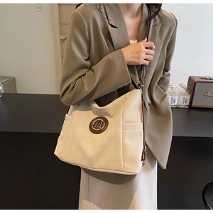 Detail of beige suede tote bag featuring a leather patch with metallic M logo and side pocket