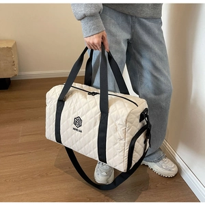 Dettaglio borsa da viaggio trapuntata beige con manici neri logati e tasca con zip