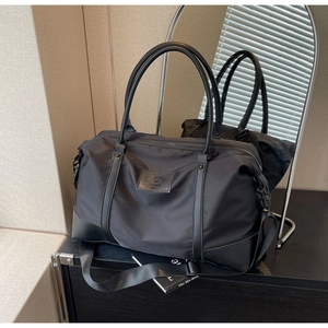 Detail of black nylon travel bag with reinforced leather handles and brand logo patch