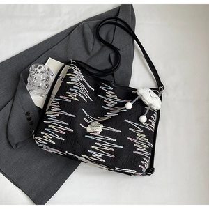 Detail of black tote bag featuring colorful wavy embroidery and a plush cloud charm