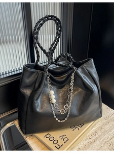 Chic black glossy leather tote bag with woven handles and pearl chain on a stone base