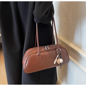 Detail of vintage brown leather baguette bag with baseball charm on model coat