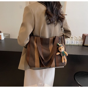 Modern striped canvas tote bag with rabbit charm shown on model in a cozy cafe setting