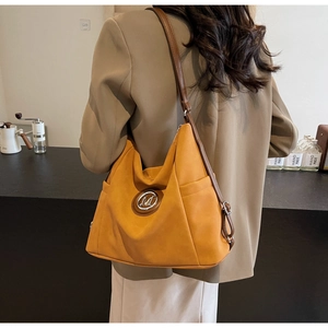 Detail of amber tote bag featuring a silver M logo and premium brown leather straps