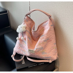 Pink tote bag detail with wave embroidery, cloud plush charm on a black leather sofa