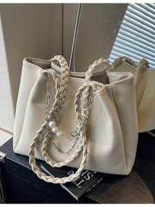 Elegant off-white leather tote bag with woven handles and pearl chain charm on mirror