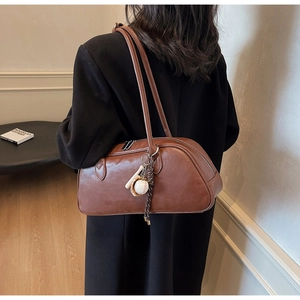 Close-up of brown vintage leather baguette shoulder bag with stylish baseball keychain charm