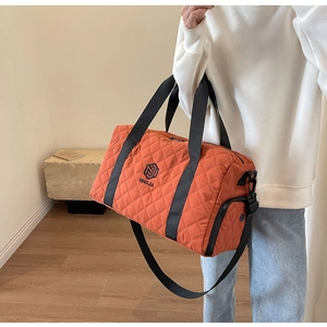 Dettaglio della borsa da viaggio trapuntata arancione brillante con manici neri e tracolla