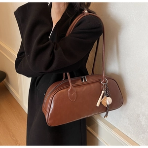 Detail of dark brown leather baguette bag featuring a baseball charm on shoulder strap