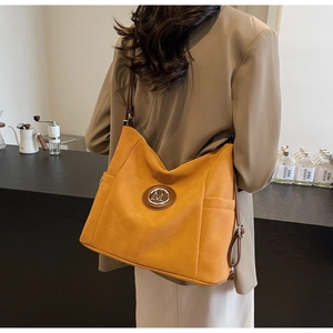 Detail view of mustard yellow suede tote bag with metal M logo and dark brown shoulder strap