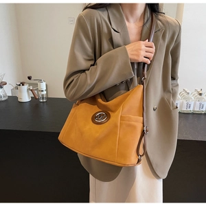 Close-up of a large orange-brown tote bag with a metal M logo on a model in a cafe