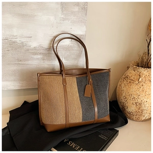 Detail view of large color-block tote bag with leather straps on a minimalist background
