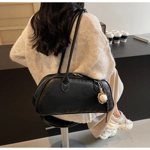 Detail of a black leather baguette shoulder bag featuring a stylish baseball charm pendant