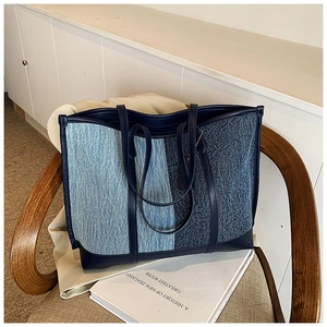 Detail of patchwork denim tote bag with navy leather straps on a wooden chair