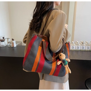 Detail of multi-color striped canvas tote bag featuring a cute teddy bear charm on the side